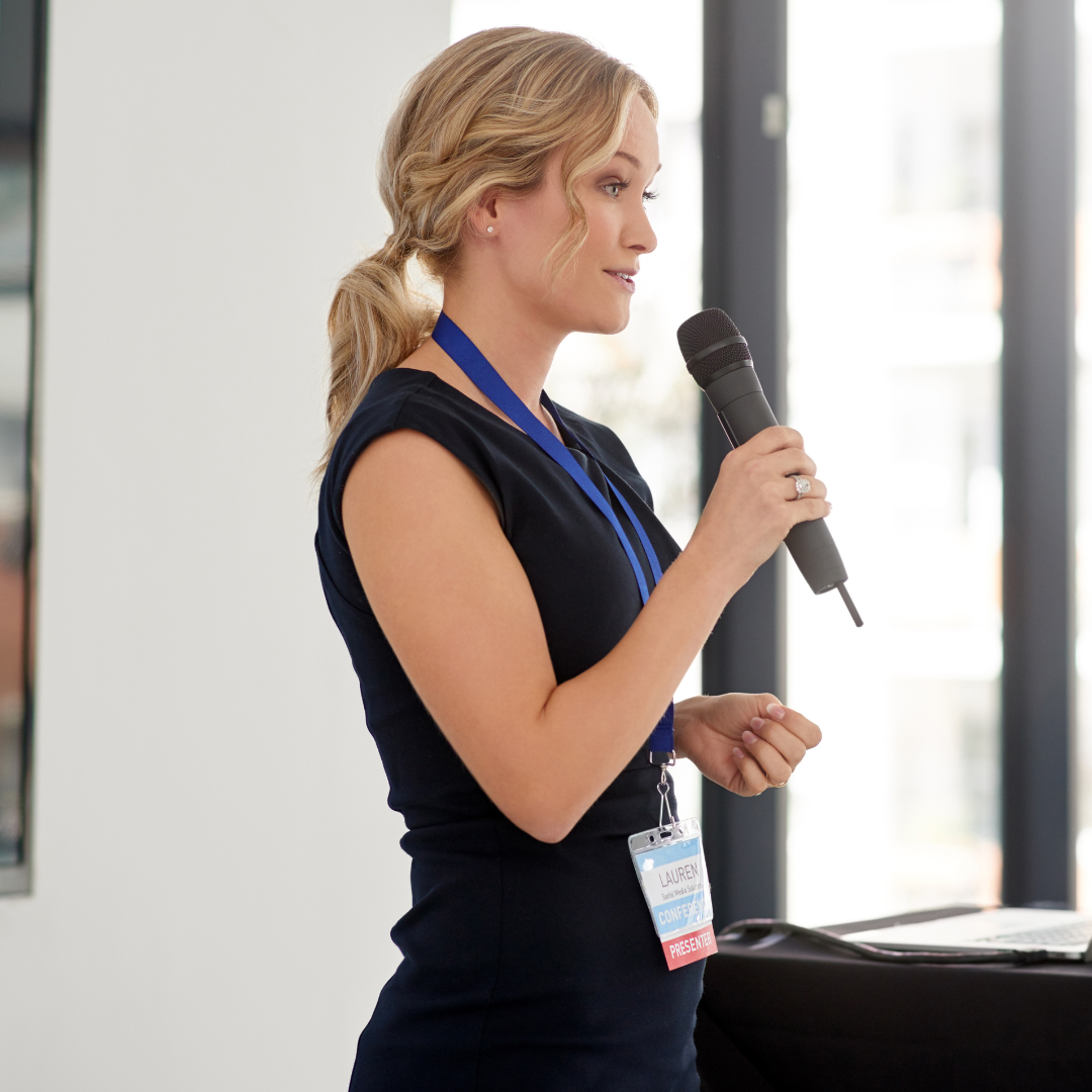 Woman presenting to an audience holding a microphone